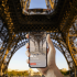 Vue du parvis de la tour Eiffel avec une main tenant un téléphone mobile